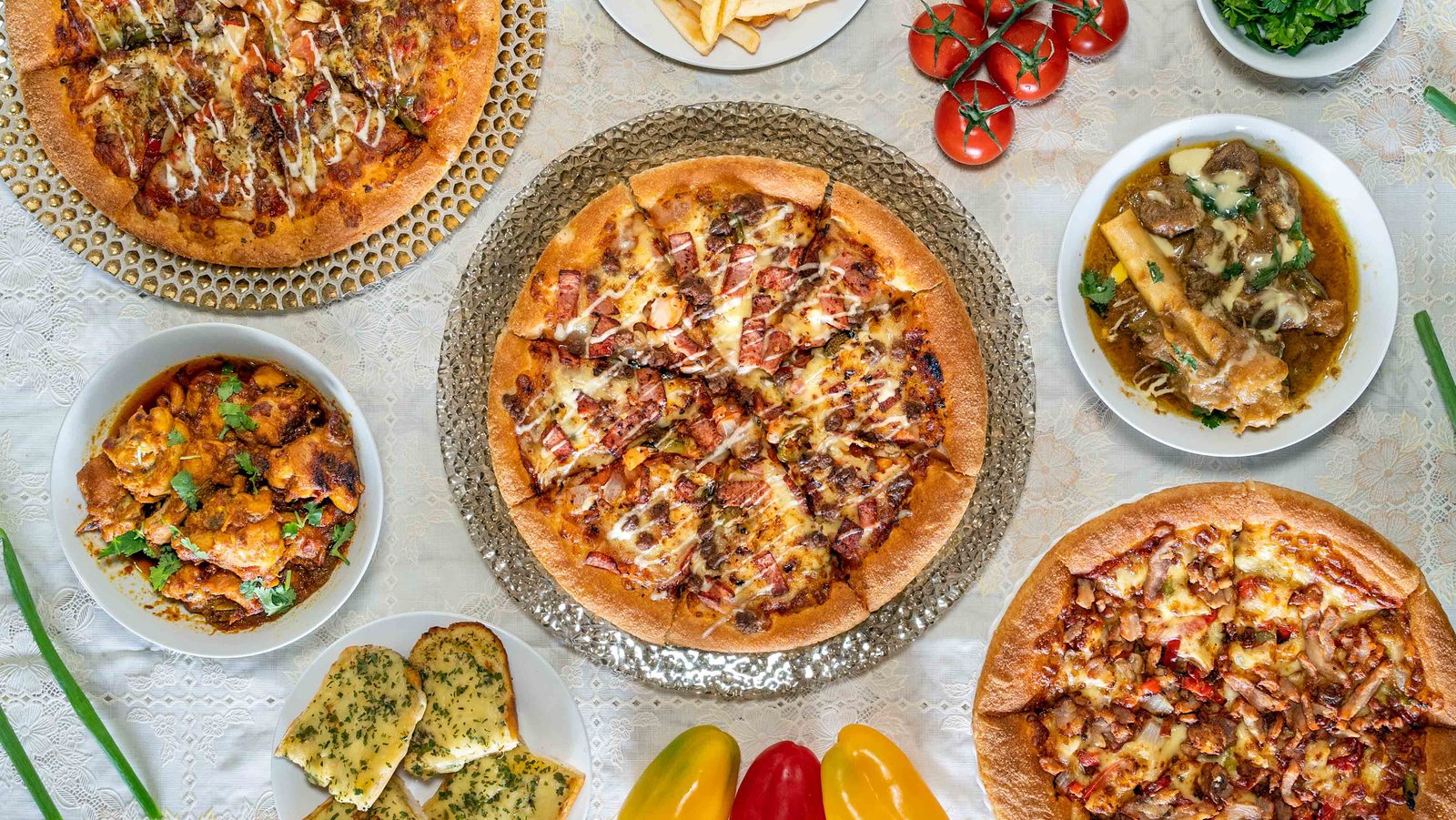 Pizzas, garlic bread and a curry laid out together on a lace tablecloth