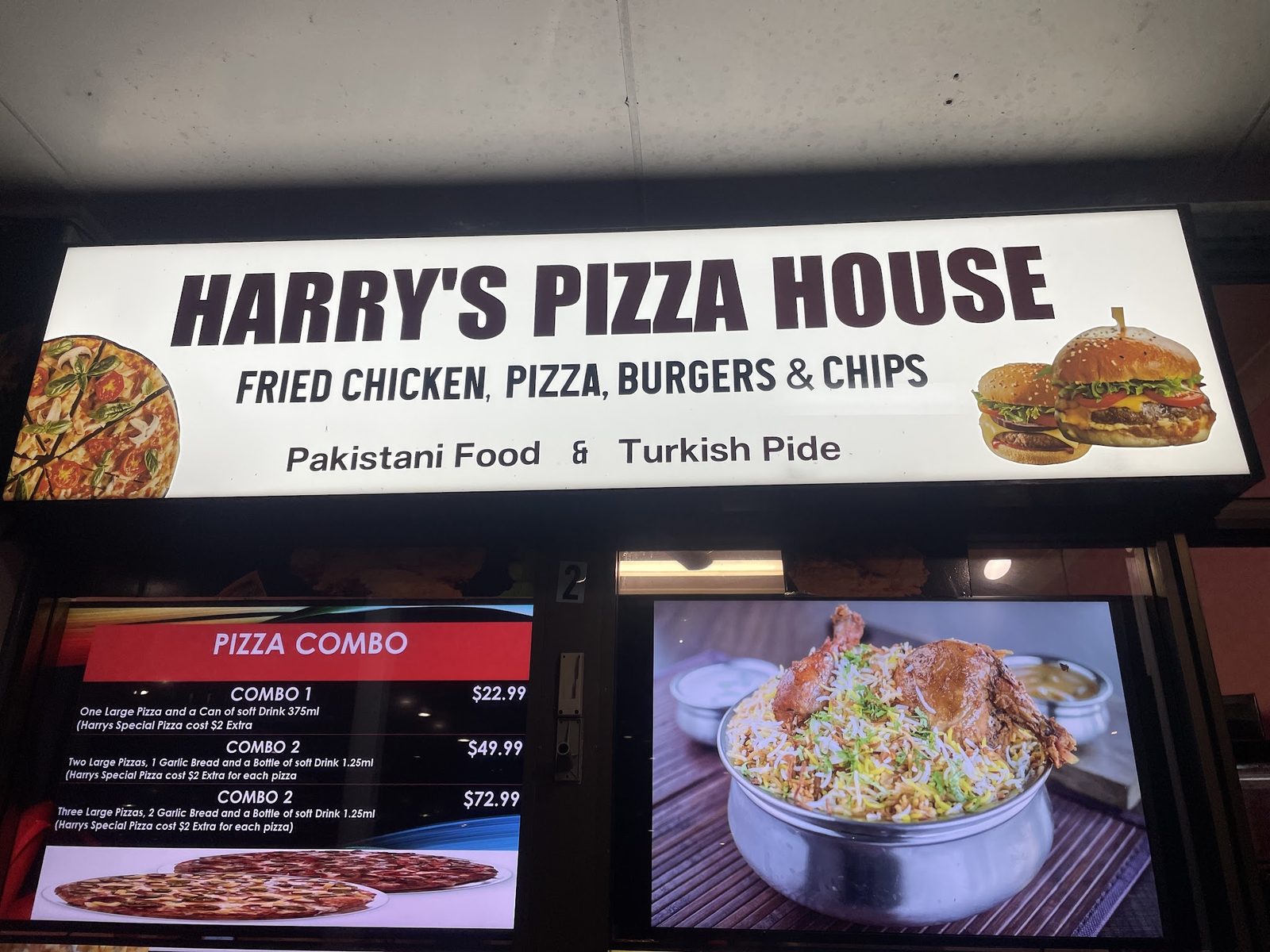 The lit Harry's Pizza House sign: fried chicken, pizza, burgers and chips, Pakistani food and Turkish pide